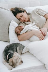 woman laying with newborn, on grey couch, dog sleeping, white pillows // Healthier Me Today