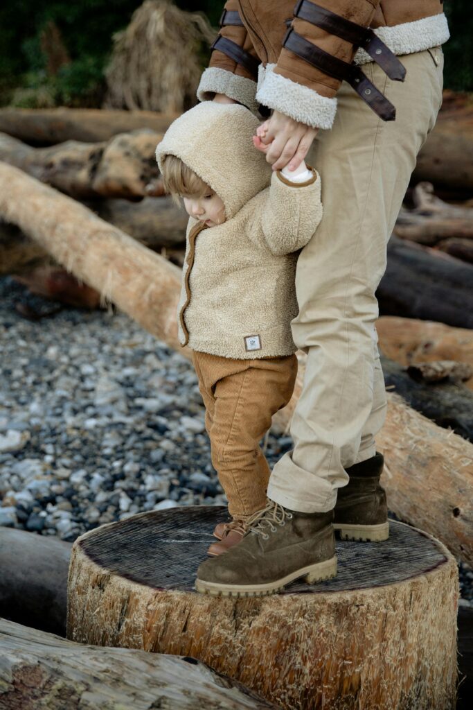 Crop person standing adorable kid on wooden logs in seashore // Healthier Baby Today 