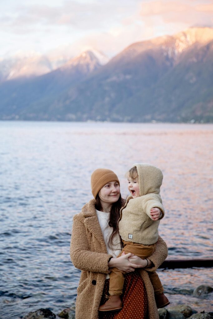 Positive mother holding cute baby during vacation near seashore in winter // Healthier Baby Today 