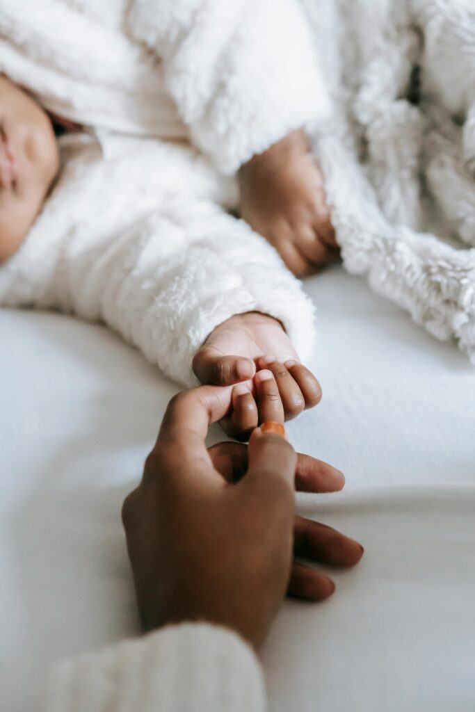 Crop anonymous black mother holding hand of baby lying on bed // Healthier Baby Today
