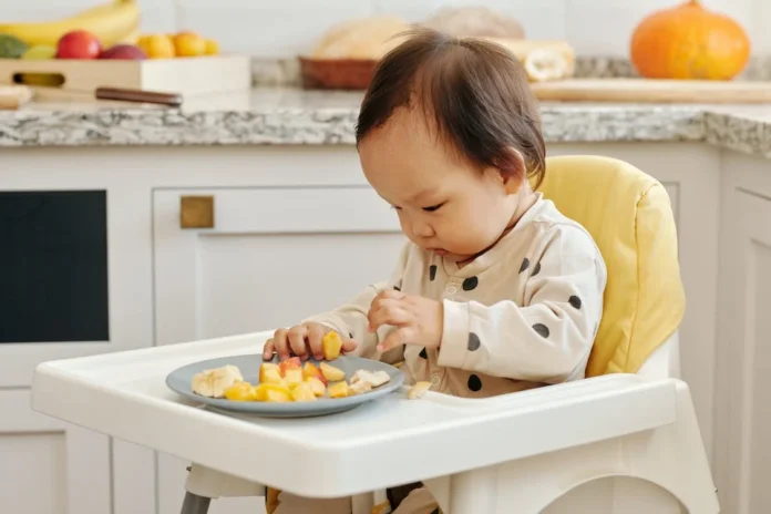 A Toddler Eating Fruits Sitting on the High Chair // Healthier Baby Today