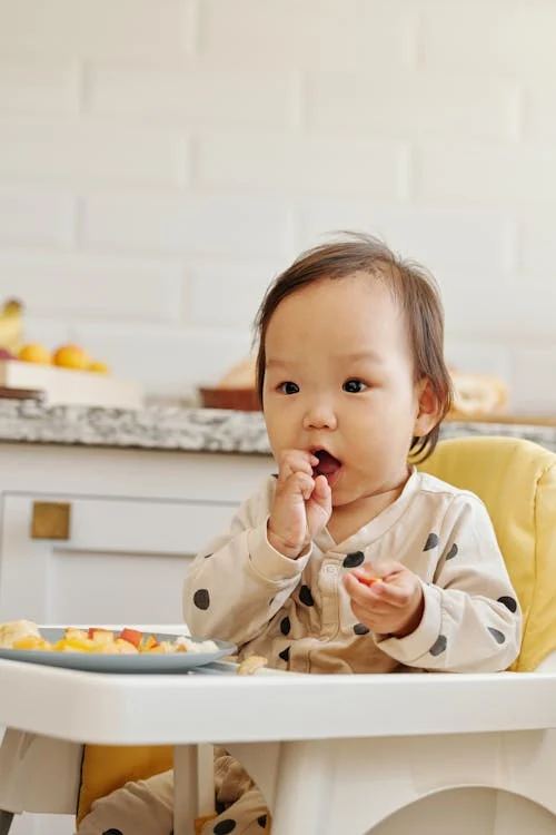 baby eating food, sitting yellow pillow // Healthier Baby Today