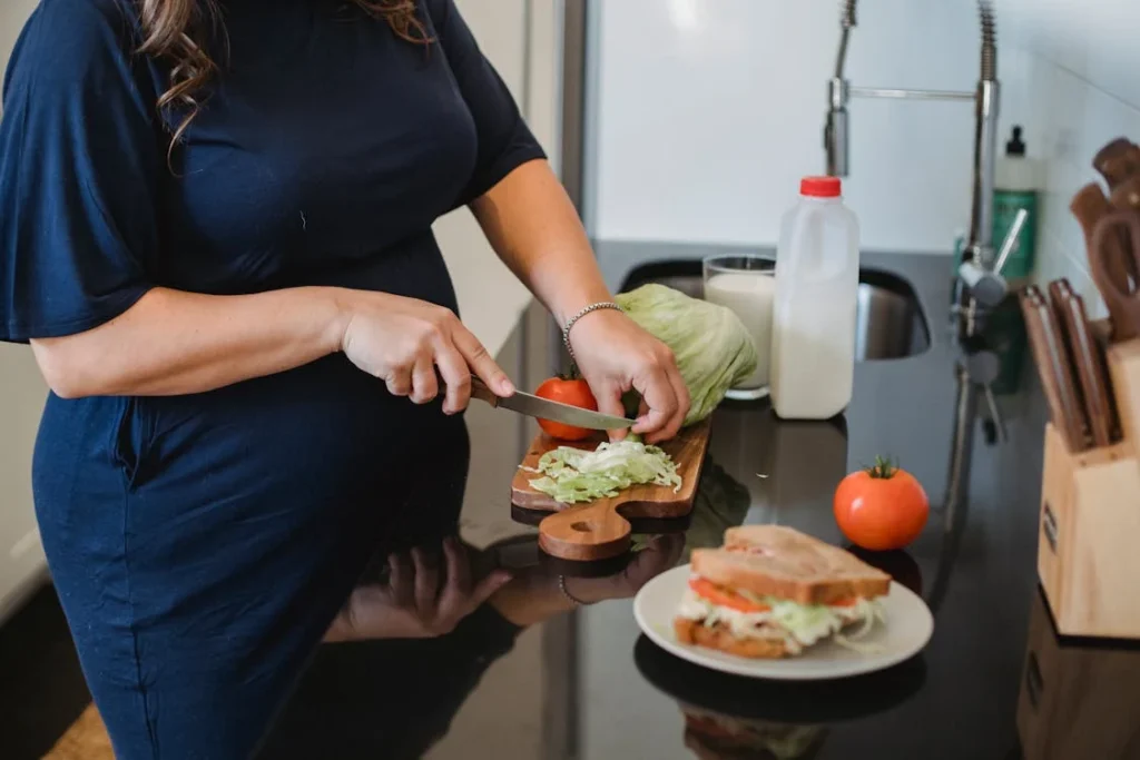 Crop pregnant woman chopping lettuce leaves in modern kitchen // Healthier Baby Today