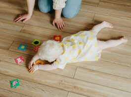 Baby Hates Tummy Time, High-Angle Shot of a Cute Baby Girl in Polka Dot Dress Lying on the Floor while Playing Toys // Healthier Baby Today