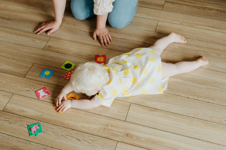Baby Hates Tummy Time, High-Angle Shot of a Cute Baby Girl in Polka Dot Dress Lying on the Floor while Playing Toys // Healthier Baby Today