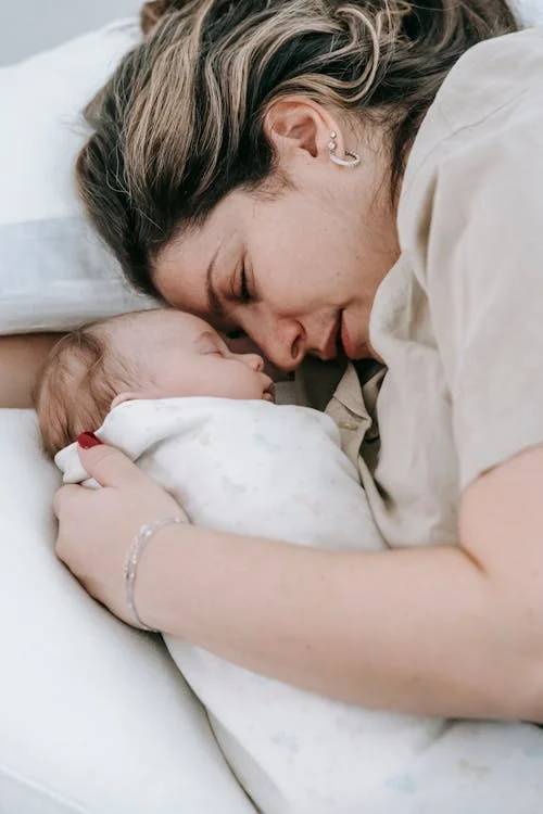 Mother with sleeping newborn baby on bed // Healthier Baby Today
