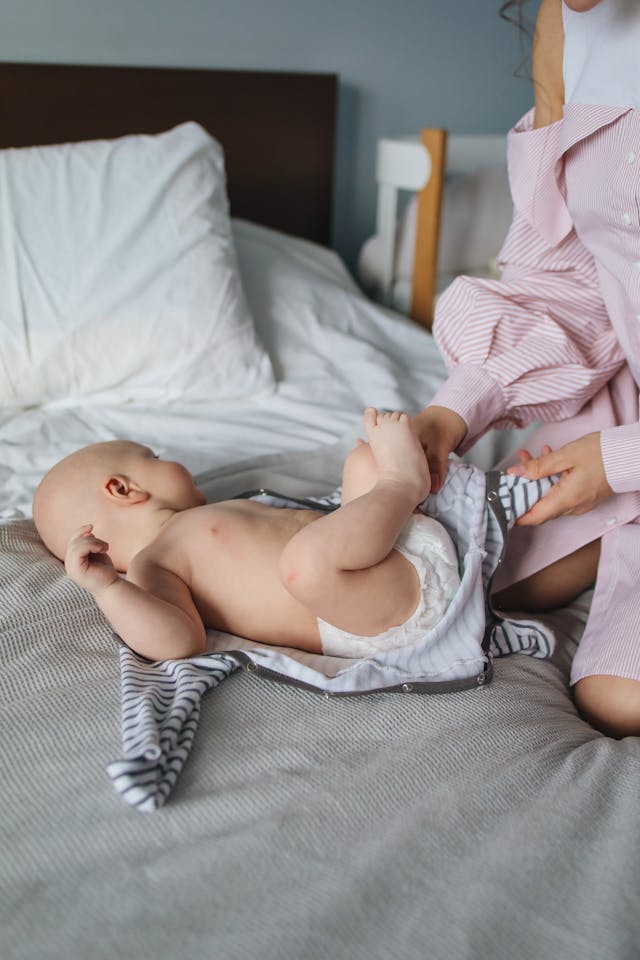 Crop woman dressing baby on bed // Healthier Baby Today