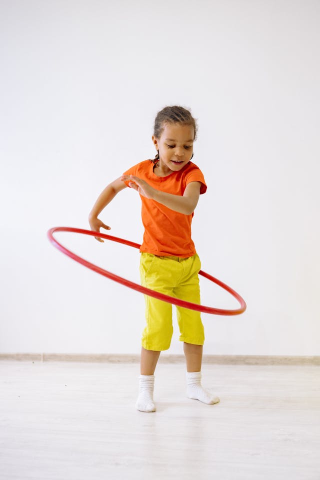 Little Girl In Orange Shirt And Yellow Pants Playing With Hula Hoop // Healthier Baby Today