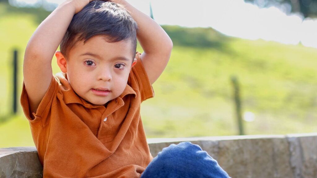 Boy with special needs sitting outdoors, wearing brown shirt and jeans // Healthier Baby Today