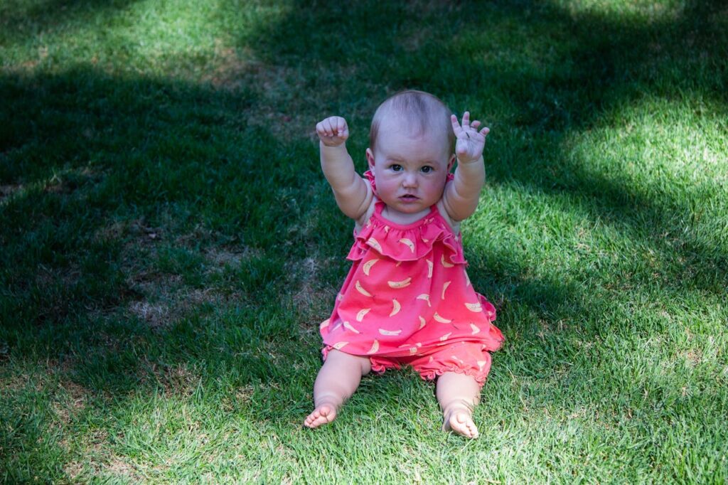 Baby Girl with Hands Raised Sitting on Green Grass // Healthier Baby Today