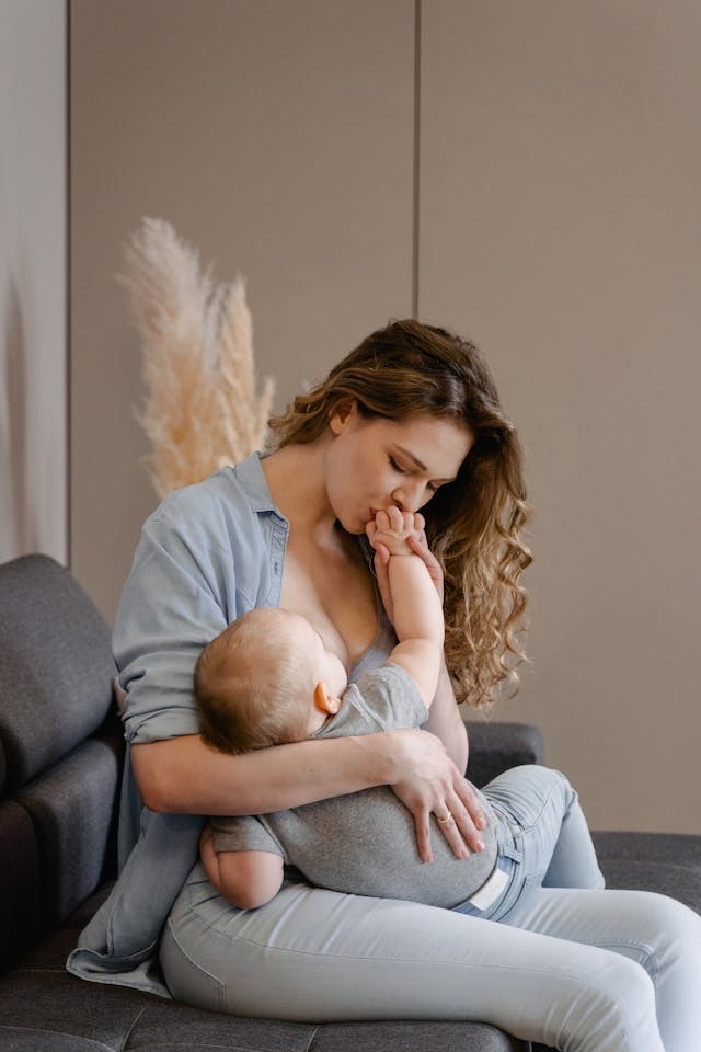 Mom holding her baby and kissing his fingers, woman has curly hair and is sitting on the sofa // Healthier Baby Today