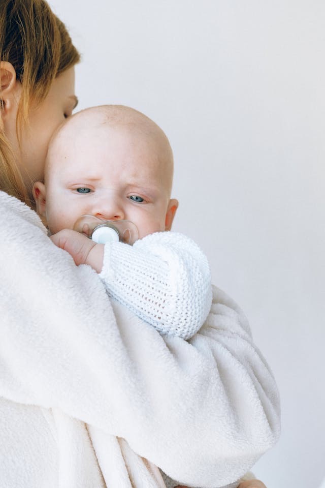 Closeup shot of baby with blue eyes, wearing white, mother is holding baby // Healthier Baby Today