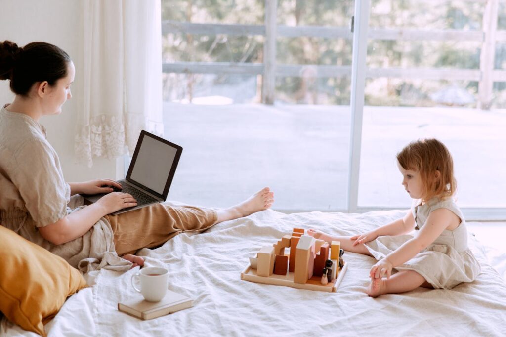 Mother using laptop while cute little girl playing on bed at home // Healthier Baby Today