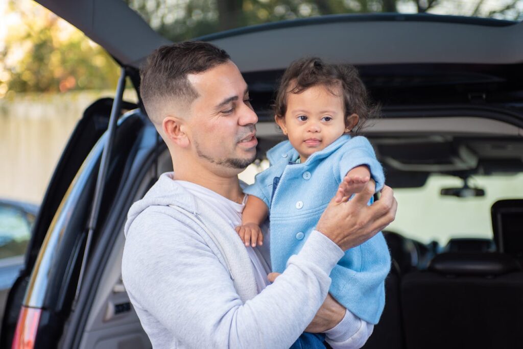 Man holding a baby standing in front of the car, baby wearing blue // Healthier Baby Today