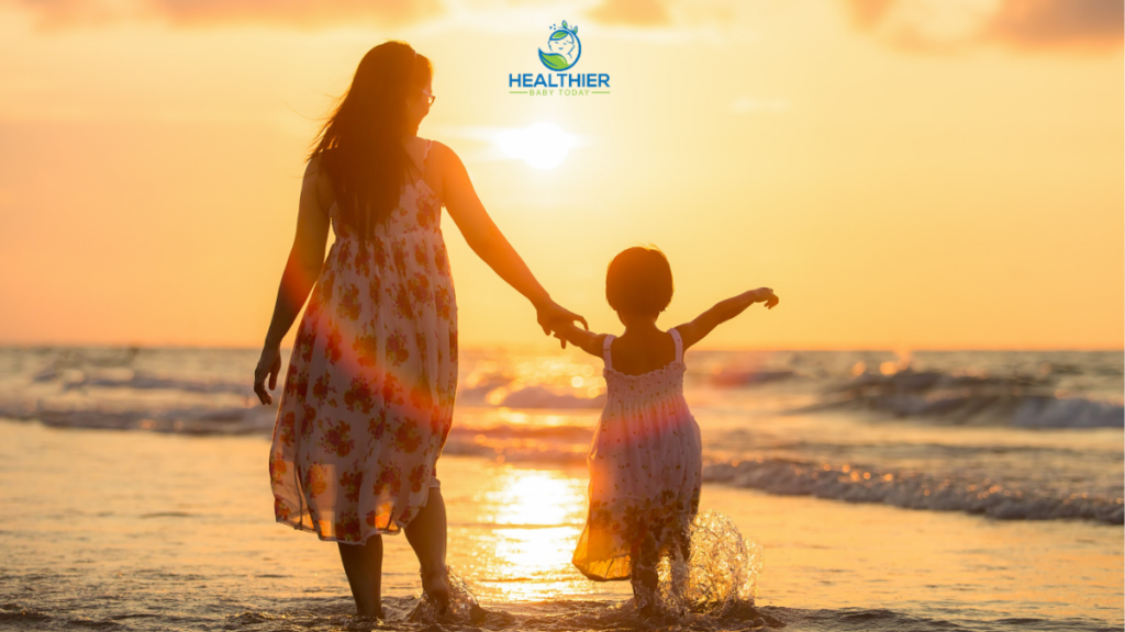 Mom and daughter standing in the ocean with a beautiful yellow sunset as their view // Healthier Baby Today