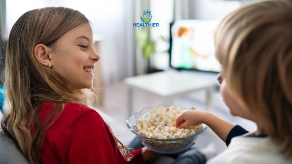 Two kids sharing popcorn while watching TV // Healthier Baby Today