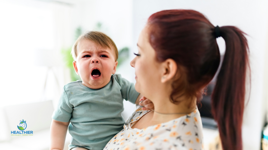 Crying baby being held by a parent while showing signs of discomfort or reflux // Healthier Baby Today